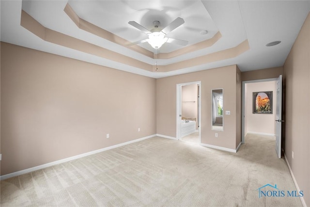 unfurnished bedroom featuring light carpet, ceiling fan, baseboards, and a raised ceiling