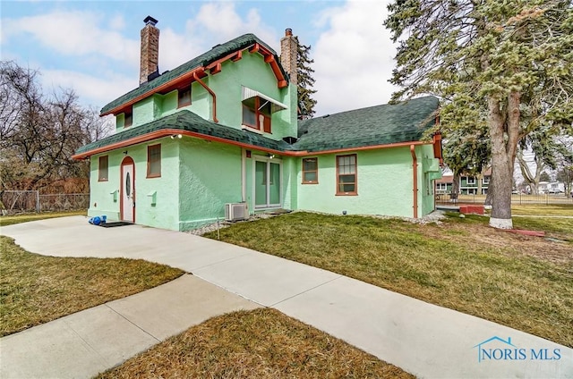 view of front of home with a front lawn, a chimney, fence, and stucco siding