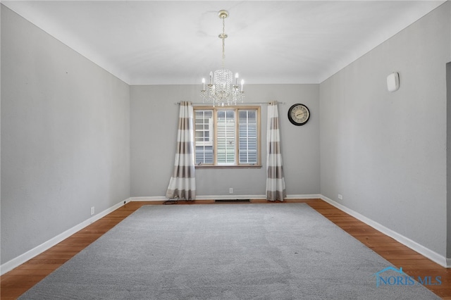 spare room featuring visible vents, a notable chandelier, baseboards, and wood finished floors