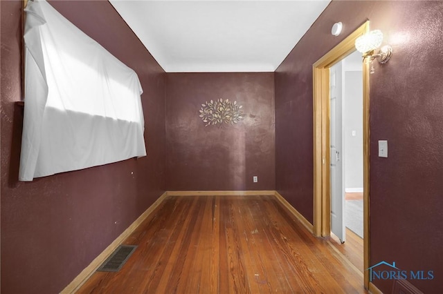 corridor featuring wood-type flooring, visible vents, and baseboards