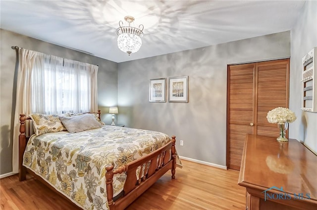 bedroom featuring light wood-type flooring, a closet, baseboards, and an inviting chandelier