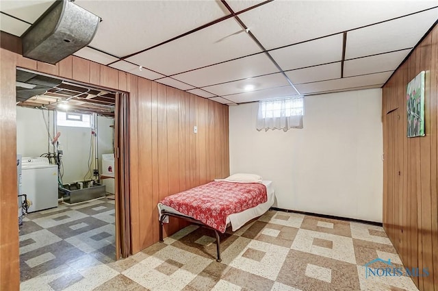 bedroom featuring a paneled ceiling, washer / clothes dryer, wood walls, and light floors