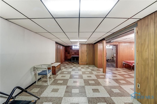 finished basement with wood walls, a drop ceiling, and light floors