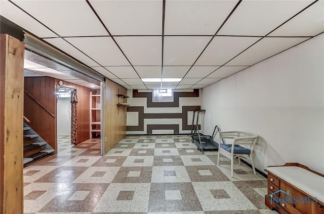 basement with tile patterned floors, a drop ceiling, wood walls, and stairs