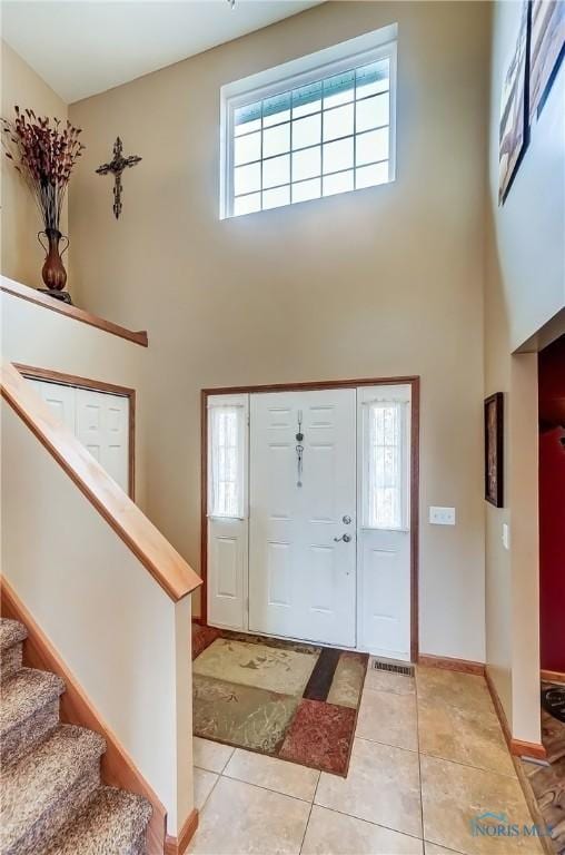 foyer entrance with stairs, light tile patterned floors, a towering ceiling, and baseboards