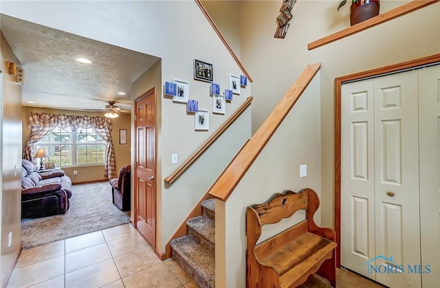 stairway with a ceiling fan, carpet, a textured ceiling, and tile patterned floors