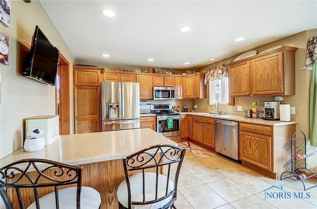 kitchen with stainless steel appliances, light countertops, a sink, and a kitchen bar