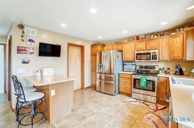 kitchen featuring stainless steel appliances, a breakfast bar, a sink, visible vents, and light countertops