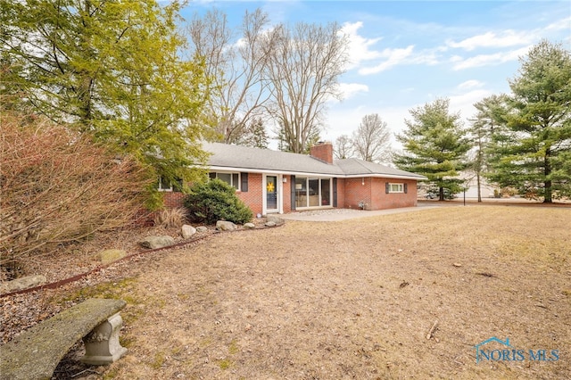 rear view of property featuring brick siding, driveway, and a chimney