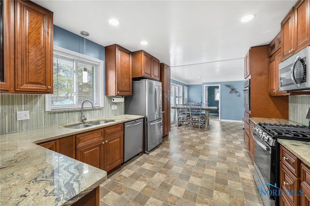 kitchen featuring brown cabinetry, light stone counters, stainless steel appliances, and a sink