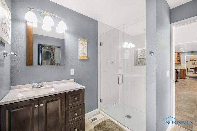 full bath featuring stacked washer / drying machine, visible vents, a textured wall, a shower stall, and vanity