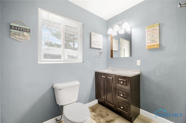 bathroom with a textured wall, vanity, toilet, and baseboards