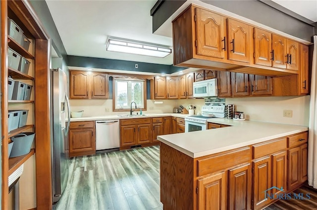 kitchen featuring a peninsula, a sink, appliances with stainless steel finishes, light wood finished floors, and brown cabinetry