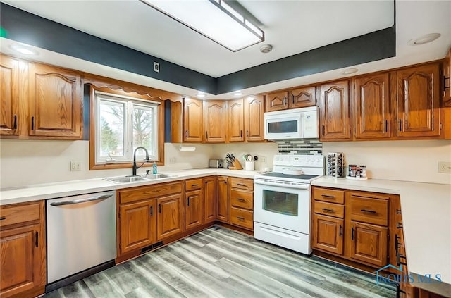 kitchen featuring white appliances, brown cabinetry, light wood-style flooring, light countertops, and a sink