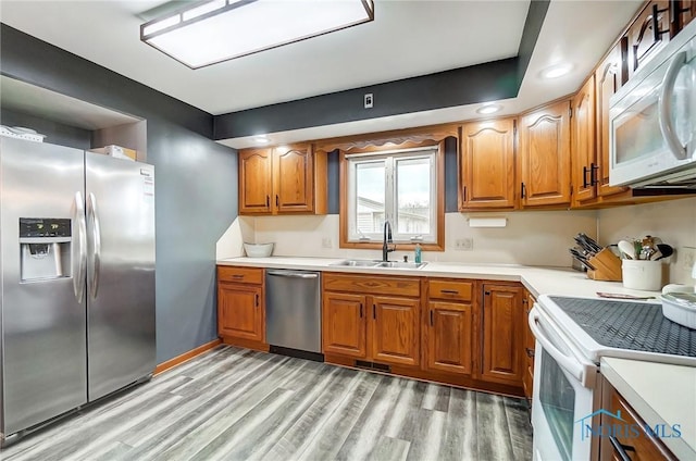 kitchen with appliances with stainless steel finishes, brown cabinets, a sink, and light wood-style flooring