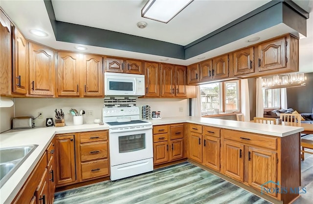 kitchen featuring brown cabinetry, white appliances, a sink, and a peninsula