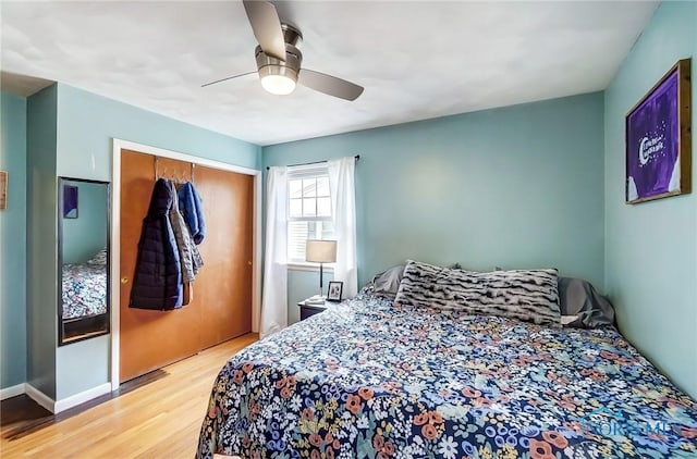 bedroom with a closet, wood finished floors, a ceiling fan, and baseboards