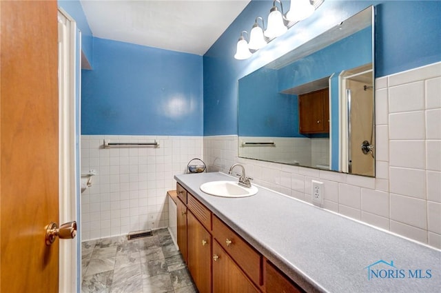 full bath with tile walls, a wainscoted wall, vanity, and walk in shower