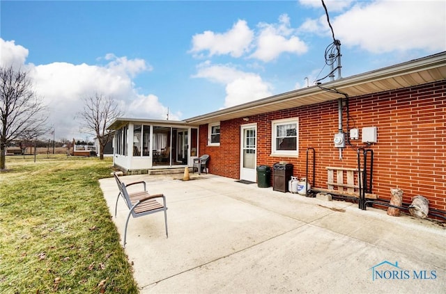 rear view of house with a patio, brick siding, a lawn, and a sunroom