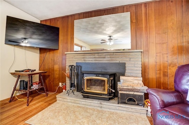 interior space with lofted ceiling, a wood stove, ceiling fan, wood walls, and wood finished floors