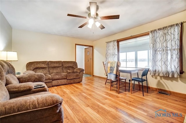 living room featuring baseboards, light wood finished floors, visible vents, and a ceiling fan