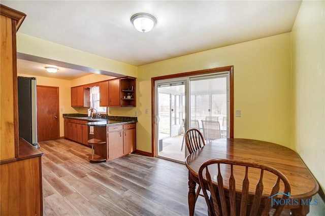 kitchen featuring brown cabinets, open shelves, light wood finished floors, dark countertops, and stainless steel fridge