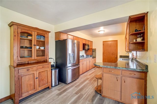 kitchen featuring light wood finished floors, open shelves, dark countertops, a sink, and black appliances