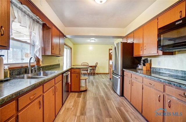 kitchen with dark countertops, black appliances, light wood finished floors, and a sink