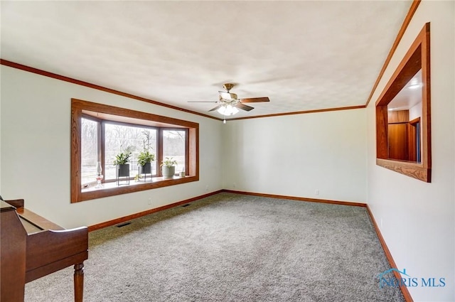 carpeted spare room with baseboards, a ceiling fan, visible vents, and crown molding