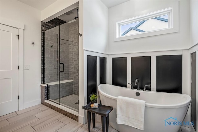 full bath featuring a freestanding tub, a shower stall, wood tiled floor, and baseboards