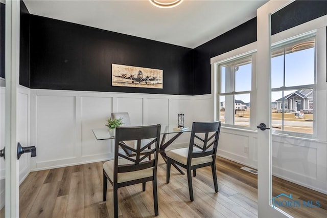 dining space featuring french doors, visible vents, a decorative wall, and light wood finished floors