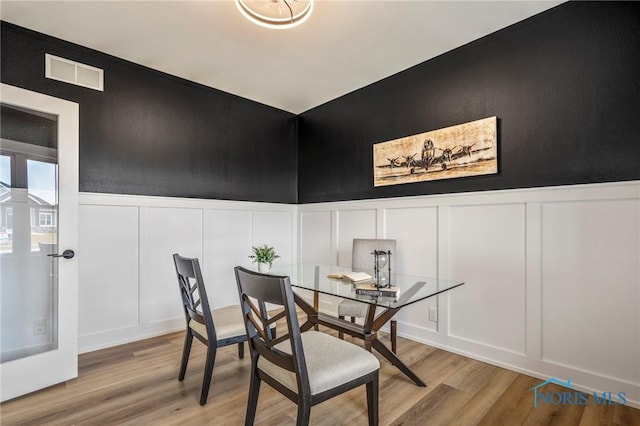 dining room with a wainscoted wall, wood finished floors, visible vents, and a decorative wall