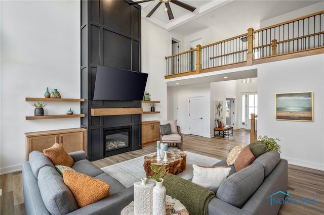 living area featuring light wood-type flooring, a fireplace, a ceiling fan, and baseboards