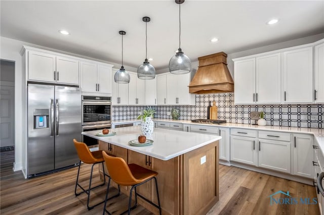 kitchen with appliances with stainless steel finishes, white cabinets, a kitchen island, and custom exhaust hood