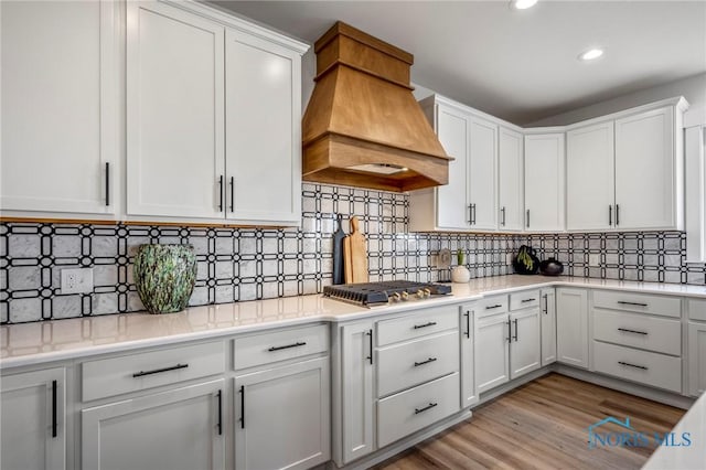 kitchen with light wood finished floors, white cabinets, custom exhaust hood, light countertops, and stainless steel gas cooktop