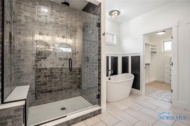 full bathroom featuring a spacious closet, a stall shower, and a soaking tub