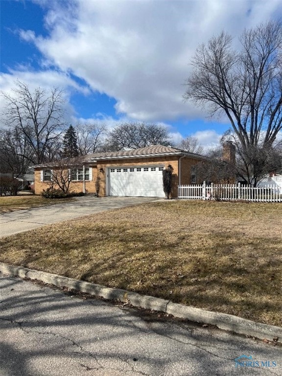 view of front of home featuring brick siding, fence, concrete driveway, a front yard, and a garage