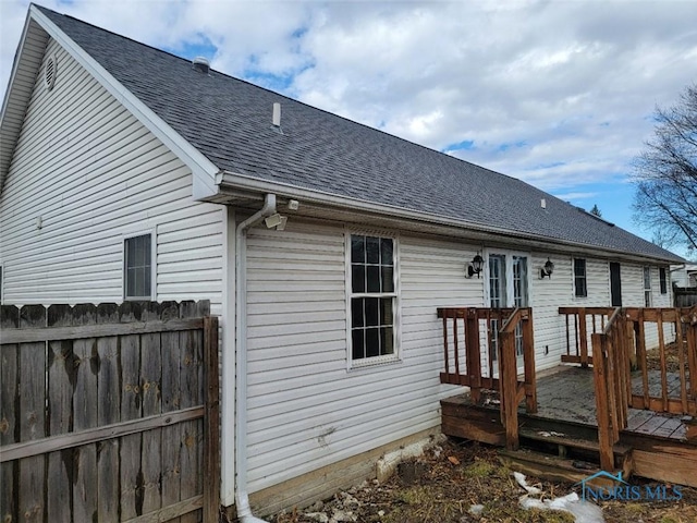 rear view of property featuring a shingled roof, fence, and a wooden deck