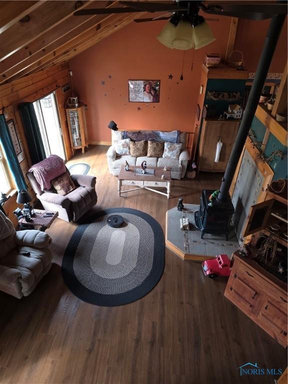 living area featuring lofted ceiling with beams, a wood stove, a ceiling fan, and wood finished floors