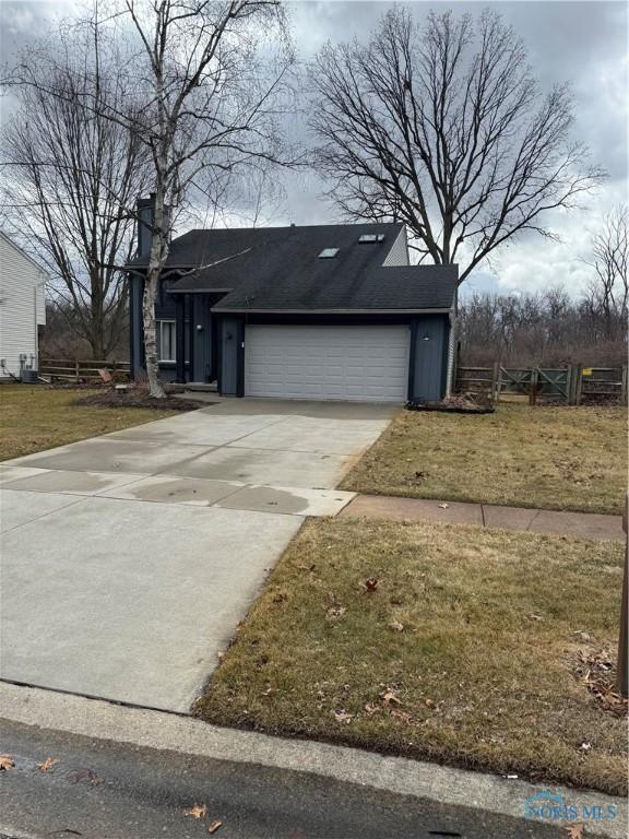 view of front of home featuring a shingled roof, an attached garage, fence, driveway, and a front lawn