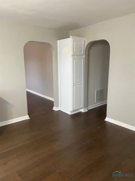 spare room featuring baseboards, arched walkways, and dark wood-style flooring