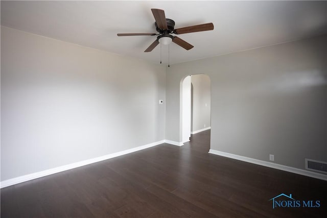 spare room with visible vents, baseboards, dark wood finished floors, arched walkways, and a ceiling fan