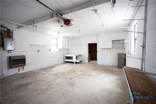 garage featuring electric panel, heating unit, a garage door opener, and concrete block wall