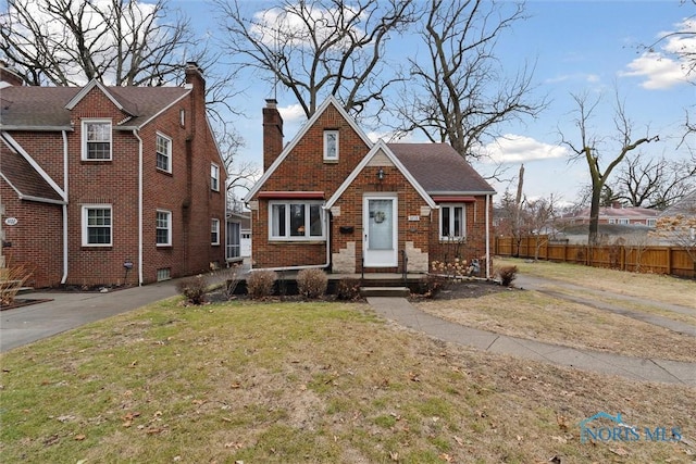 view of front of house with a front yard, brick siding, fence, and a chimney