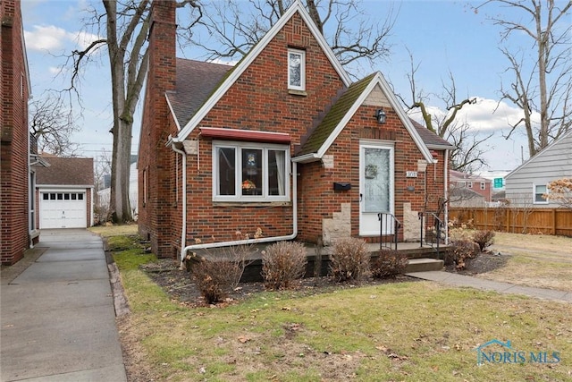 tudor-style house featuring an outbuilding, brick siding, fence, concrete driveway, and a chimney