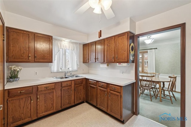 kitchen with ceiling fan, a sink, light countertops, light floors, and brown cabinetry