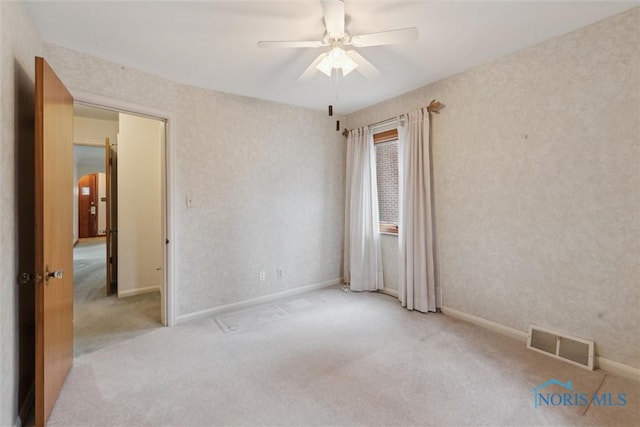 carpeted empty room with baseboards, visible vents, and a ceiling fan