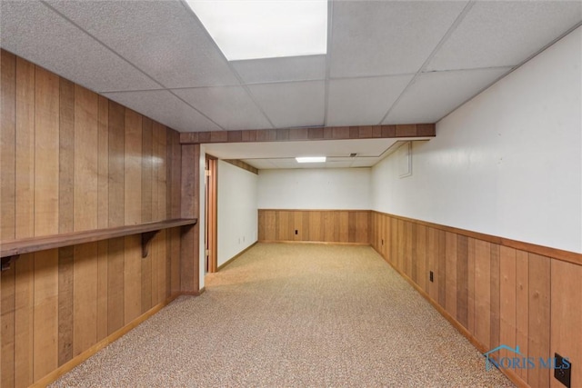 finished basement with light colored carpet, a wainscoted wall, wood walls, and a drop ceiling