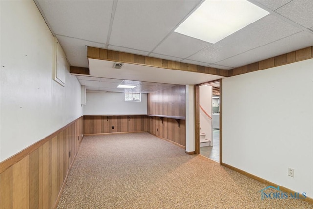 below grade area featuring carpet floors, a paneled ceiling, visible vents, wainscoting, and wooden walls