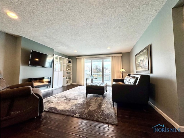 living area with a textured ceiling, wood finished floors, built in features, baseboards, and a glass covered fireplace